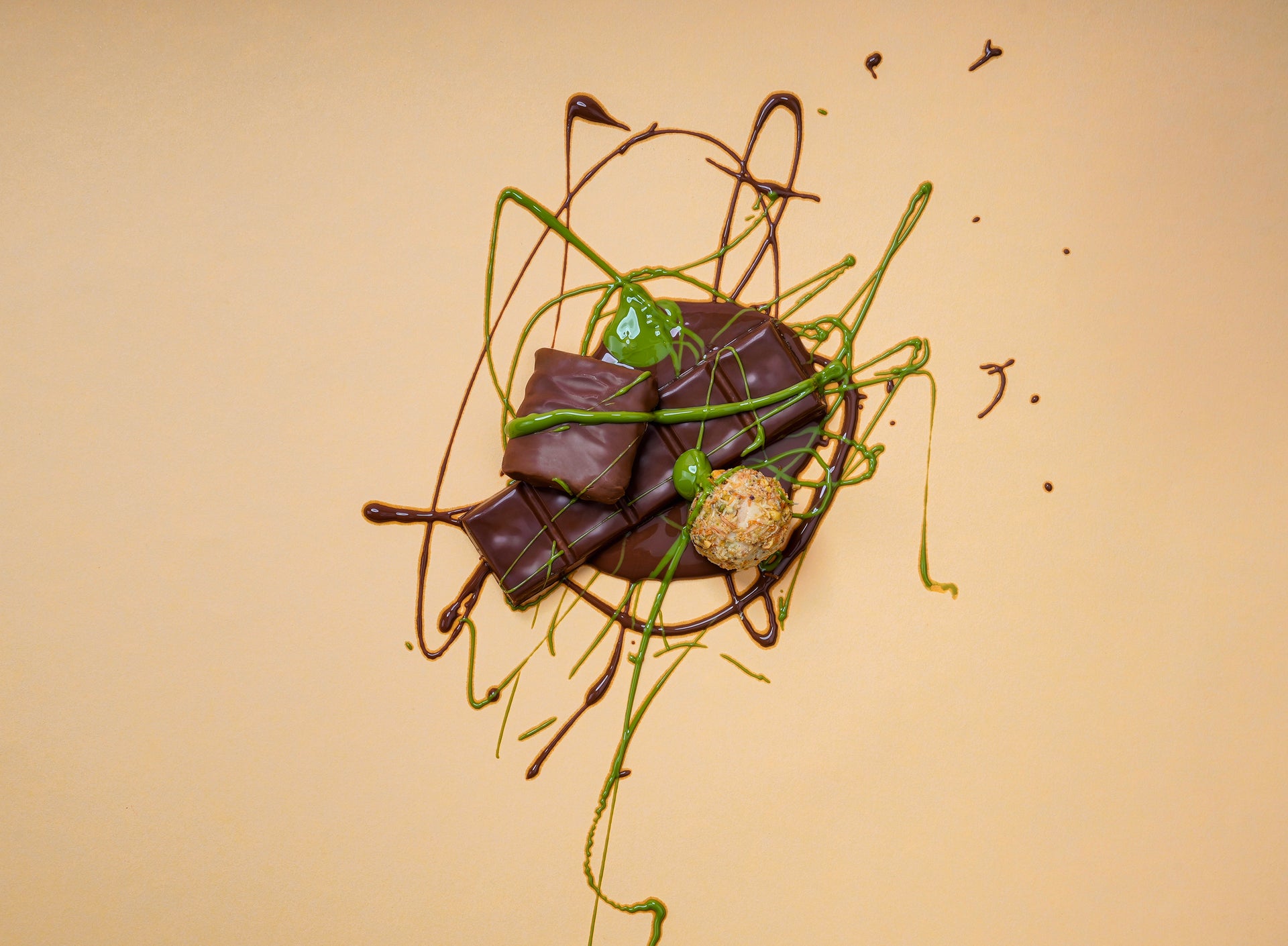 Artistic presentation of Snacksify chocolates with pistachio and chocolate sauces on a beige background